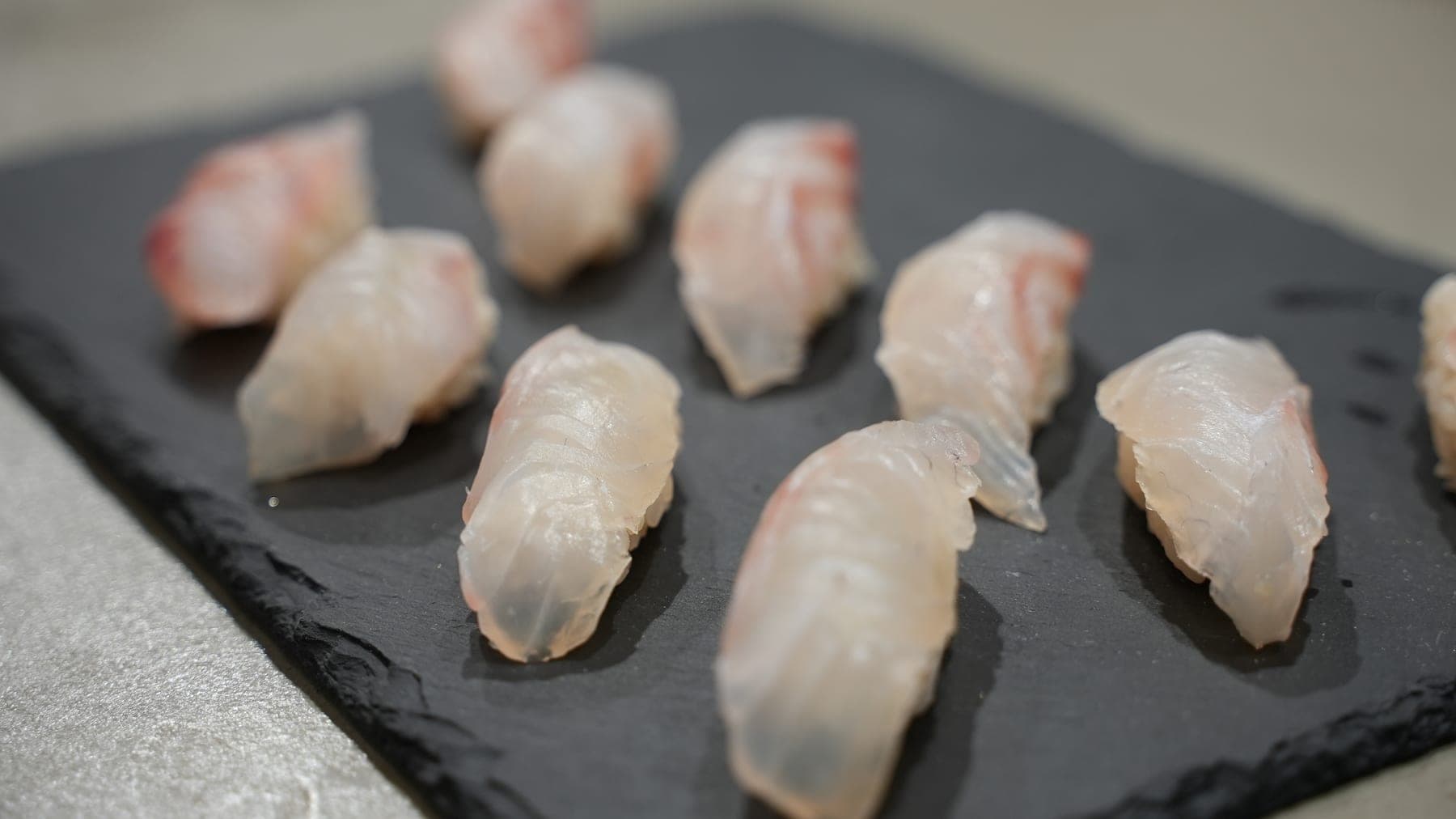 黒いスレートの上に並べられた、握りたての白身魚の握り寿司