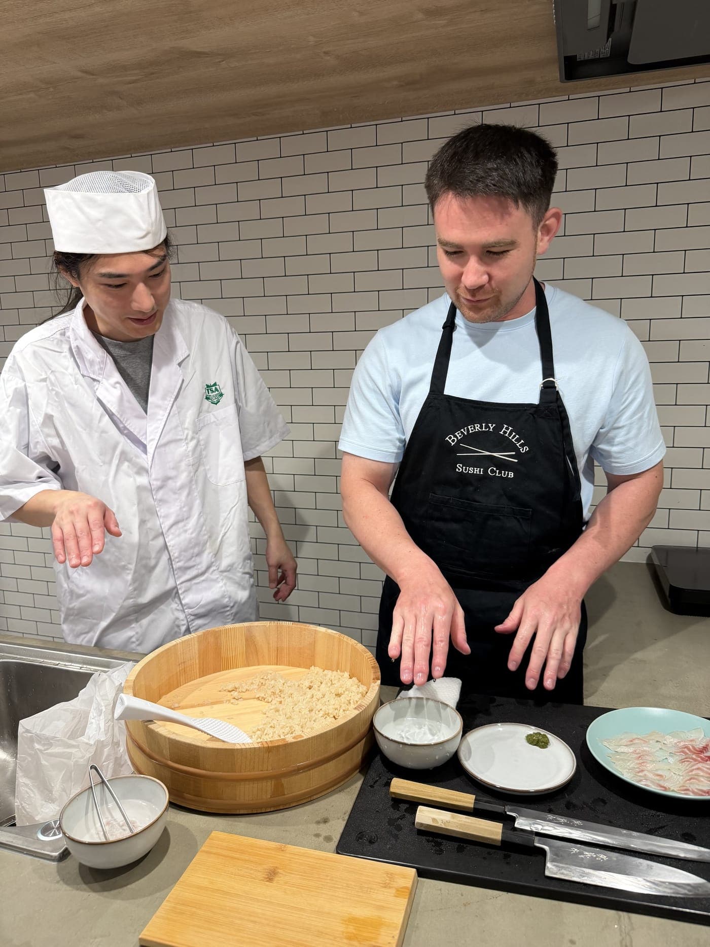 半切りに広げたシャリと、ネタ・包丁を前に手ほどきをする職人